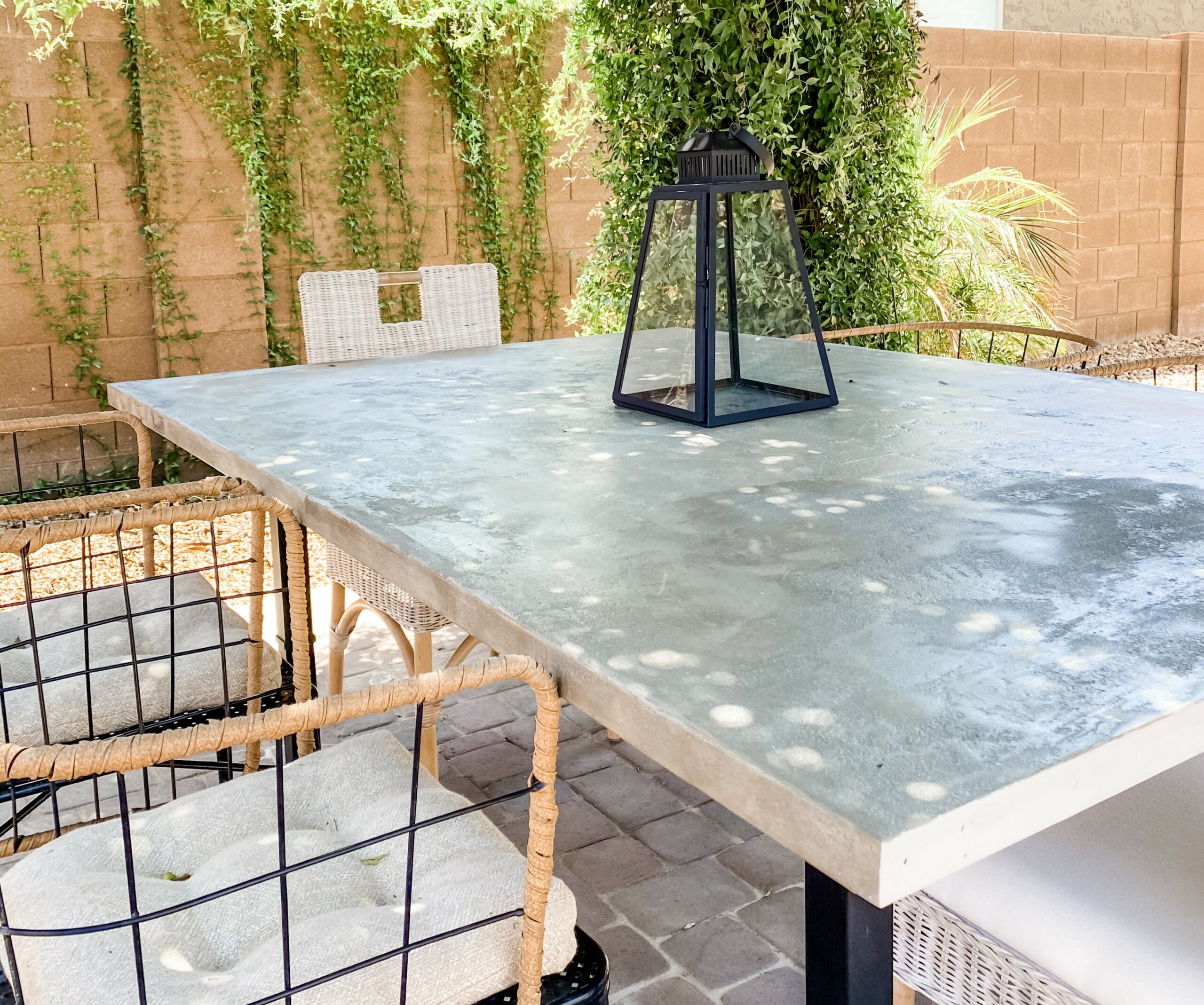 A concrete patio table with wicker chairs and a lantern, featuring a sturdy concrete table top