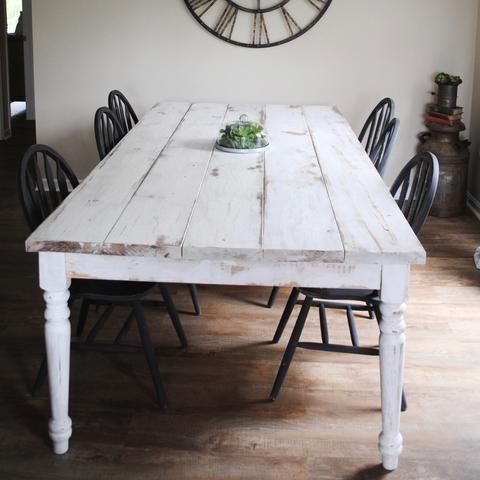 A whitewashed farmhouse table surrounded by black chairs, complemented by a clock