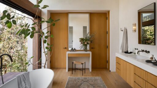 A bathroom with wooden flooring and a large window, providing ample natural light