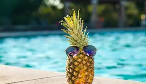 Free Tropical pineapple wearing sunglasses by a sunny swimming pool, perfect for vacation vibes. Stock Photo
