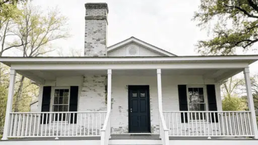 full house exterior with lime-washed white brick, weathered texture, moss streaks, front porch visible