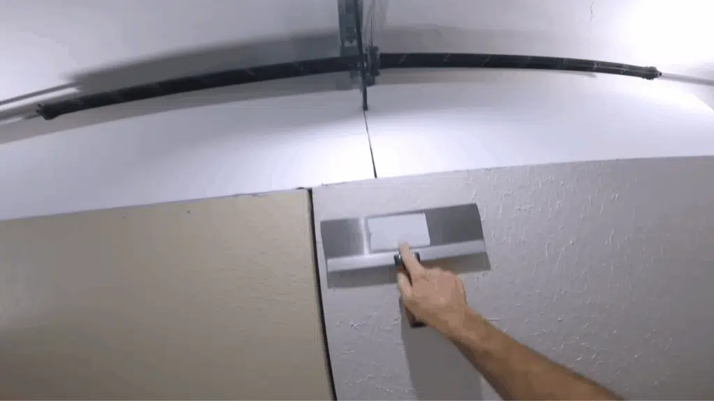 14-inch drywall knife being used to smooth out excess joint compound after the first coat has dried, creating an even surface