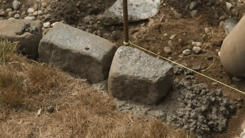 Cobblestones being placed along the edge of the dug pathway to create a defined border.