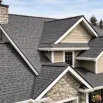 Modern house with gray asphalt shingle roof, multiple gables, and chimney in a suburban setting