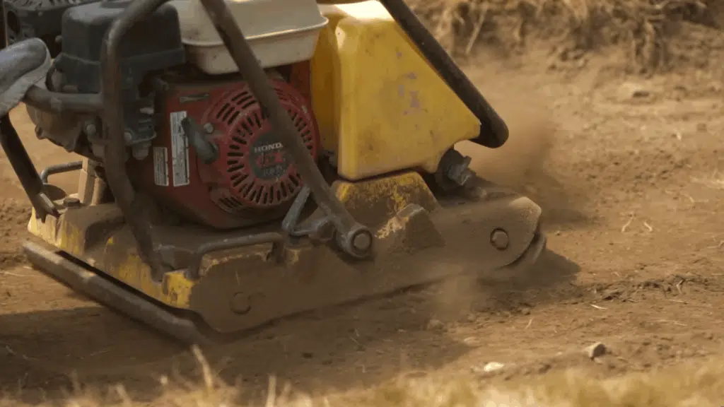 Motorized plate compactor being used to compact the soil along the dug pathway to create a stable base.