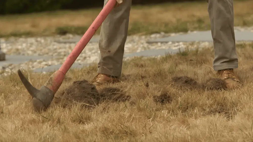 Person using a mattock to dig a trench for a walkway, clearing the topsoil.