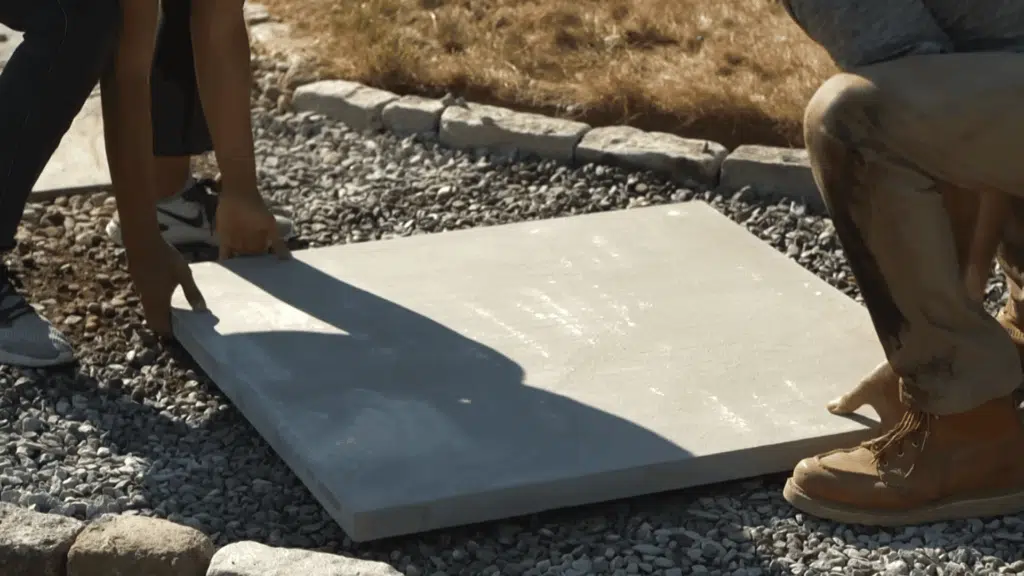 Two people placing large concrete pavers onto the gravel, positioning them evenly along the walkway.