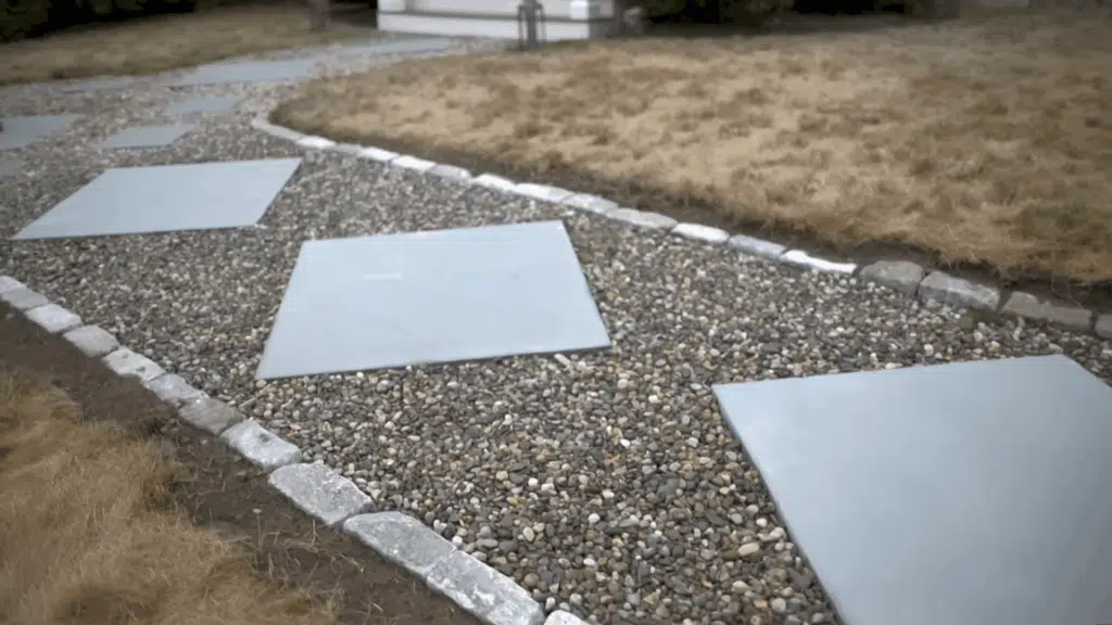 View of a completed pea gravel walkway with evenly spaced concrete pavers, bordered by cobblestones.