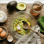 a flat lay of natural diy hair mask ingredients including coconut oil eggs honey and avocado arranged neatly on a wooden surface