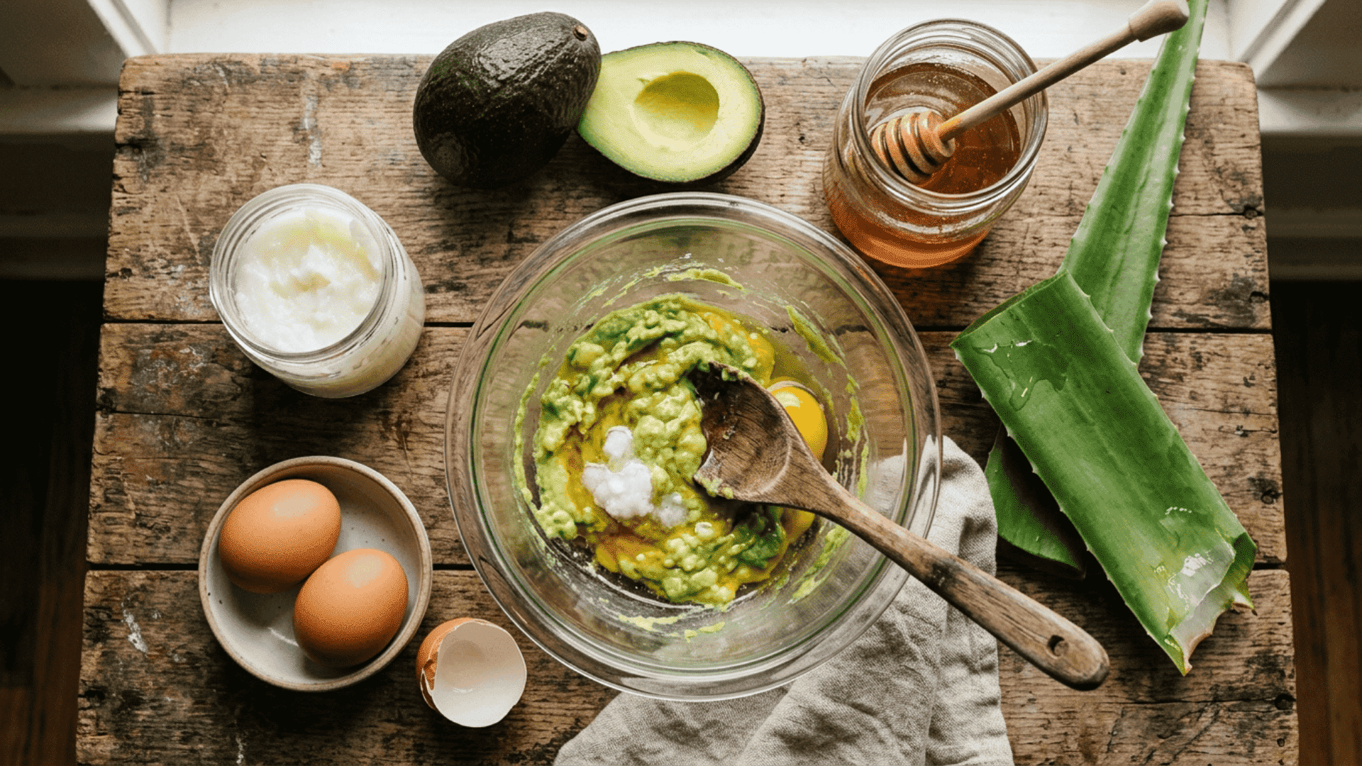 a flat lay of natural diy hair mask ingredients including coconut oil eggs honey and avocado arranged neatly on a wooden surface