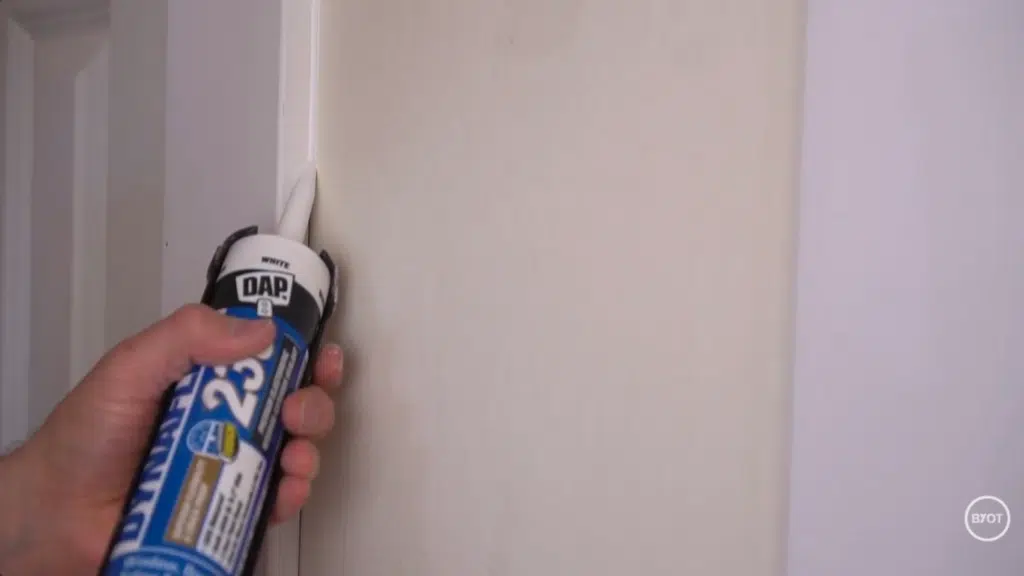 a person using a caulk to seal spaces in the wall in a room