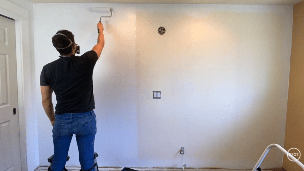 a person using a paint roller to paint a wall in a room