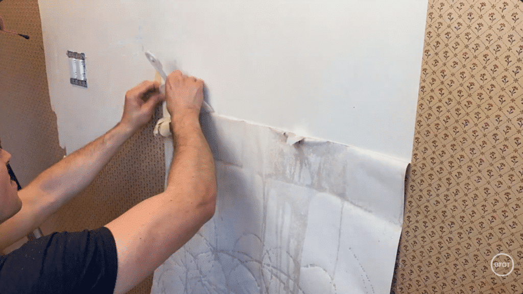 a person using a putty knife to scrape off the wallpaper in a room