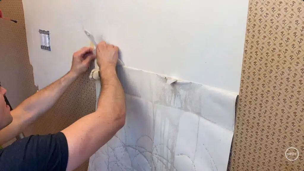 a person using a putty knife to scrape off the wallpaper in a room
