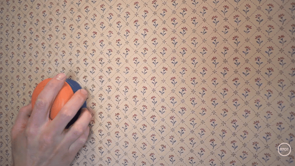 a person using scoring tool to score the surface of the wallpaper in a room
