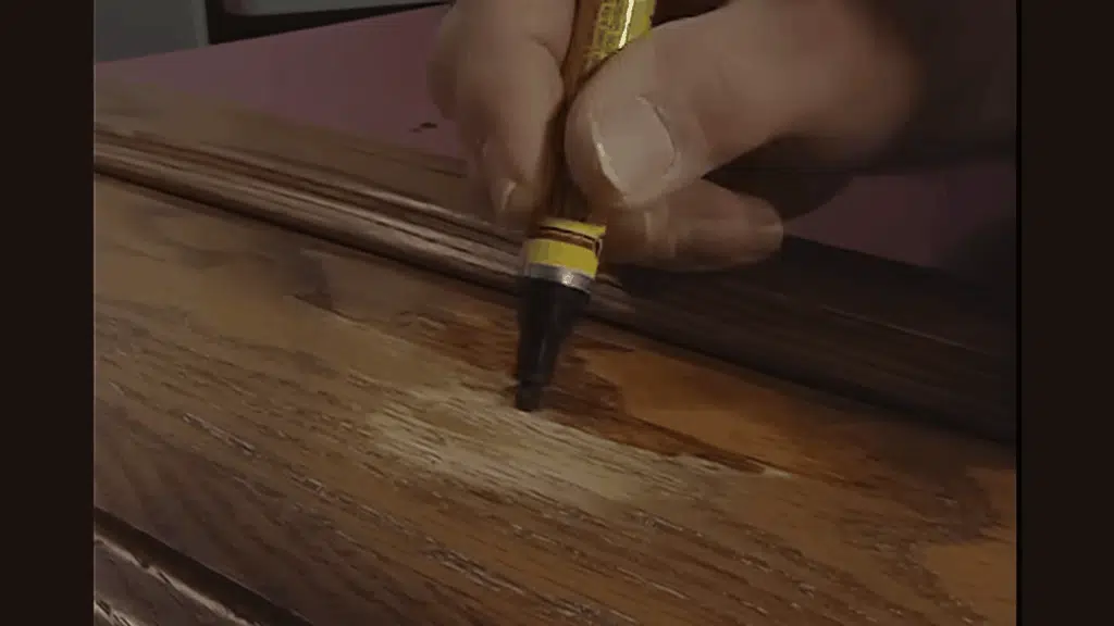 applying wood touch-up marker to fix worn cabinet surface.