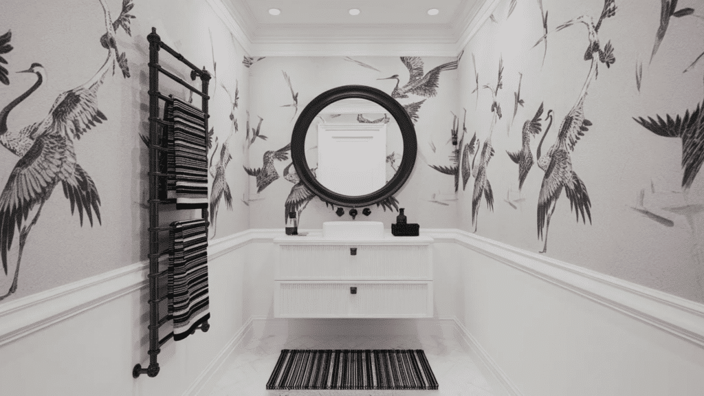 black and white bathroom with crane print wallpaper, striped towels, floating vanity, and round black mirror creating a stylish design.