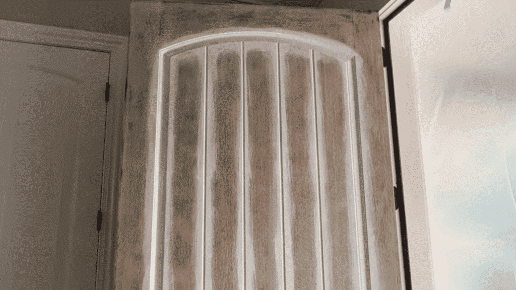 brush applying white primer onto a door panel's beveled edge