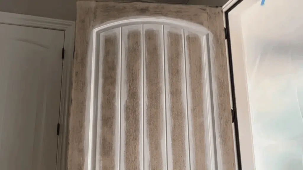 brush applying white primer onto a door panel's beveled edge