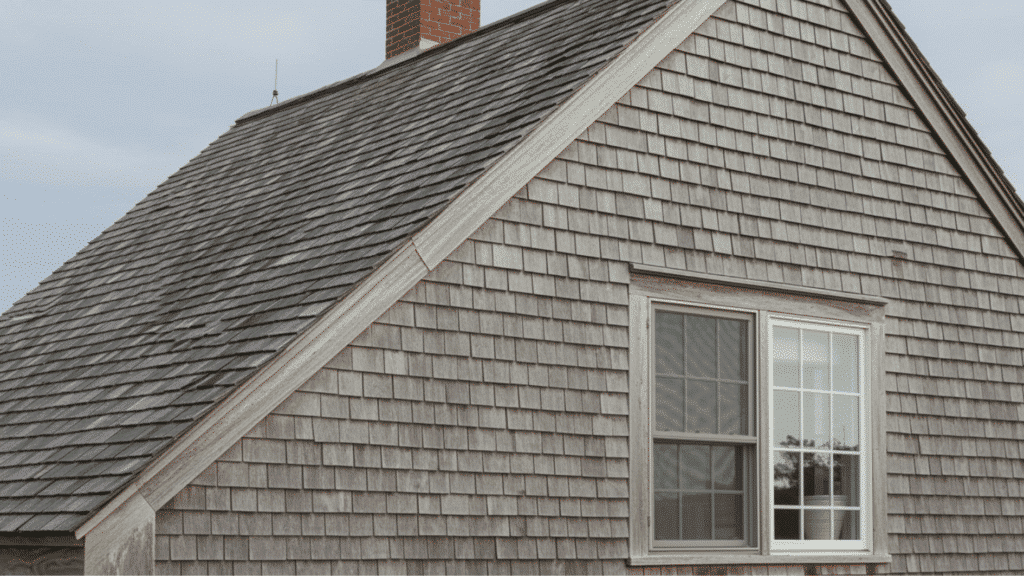 cape cod style house exterior with weathered cedar shingles, pitched roof, chimney, and traditional coastal design