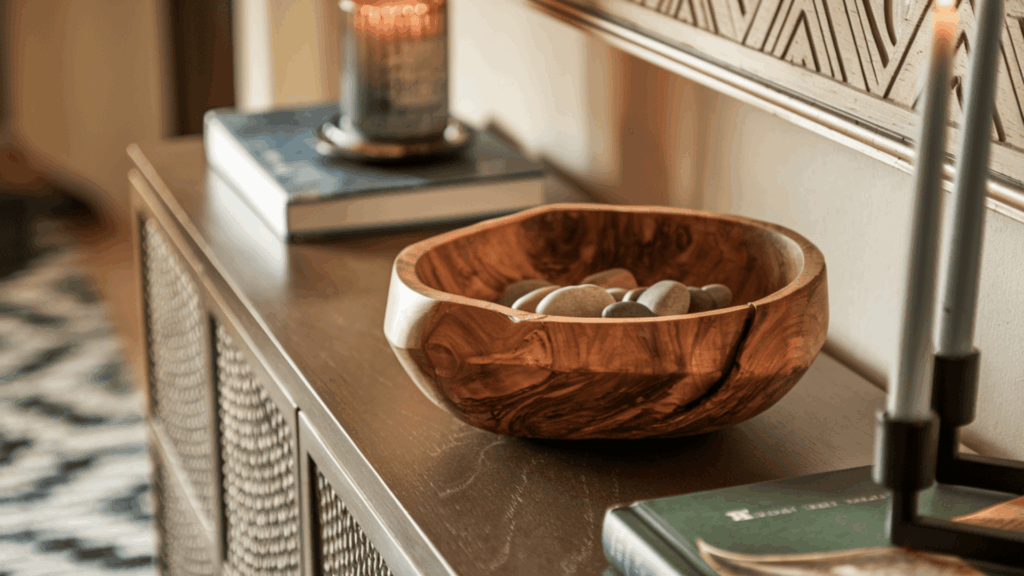 carved wooden bowl with natural grain texture placed off-center on a console table with smooth decorative stones inside