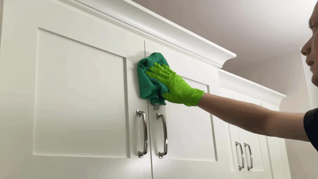 cleaning cabinet surface with microfiber cloth in kitchen.