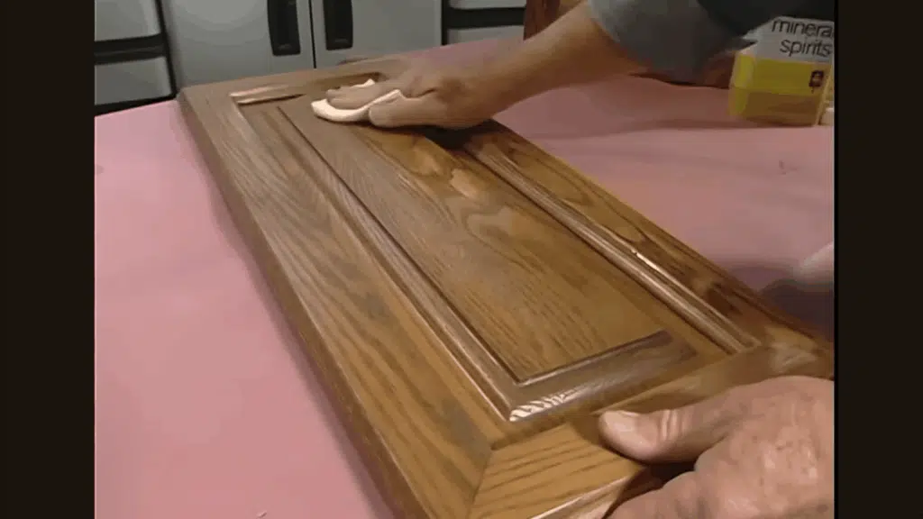 cleaning wooden cabinet door surface with cloth and mineral spirits.