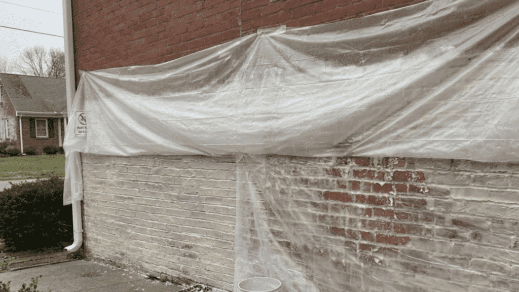 clear plastic film drapes over a brick wall coated in a thick semi transparent paint stripping compound