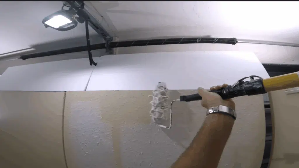 close-up of a paint roller being used to spread joint compound smoothly on the wall, with light pressure to avoid lines