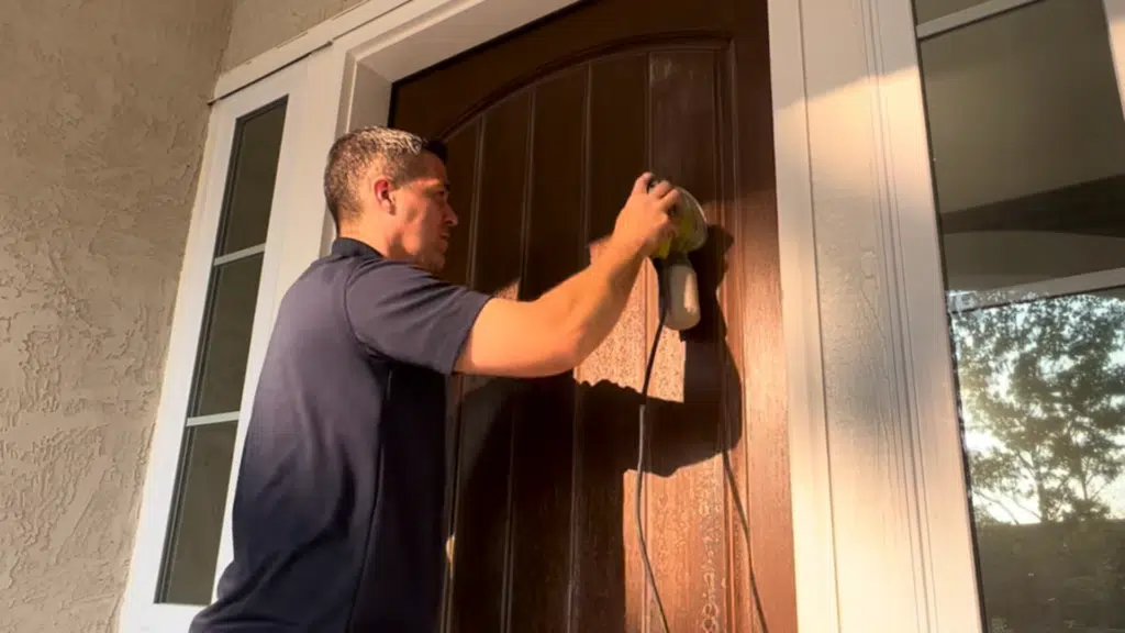 close-up of an orbital sander removing blue paint from a flat door panel