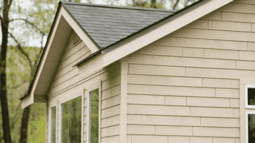 close-up view of a house corner featuring beige vinyl siding with a dark roof, showcasing a clean, modern design and large windows