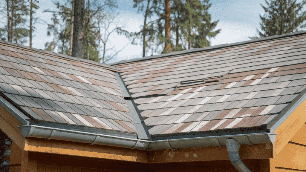 composite roof shingles in mixed gray and brown tones on residential home with metal gutters and forest backdrop