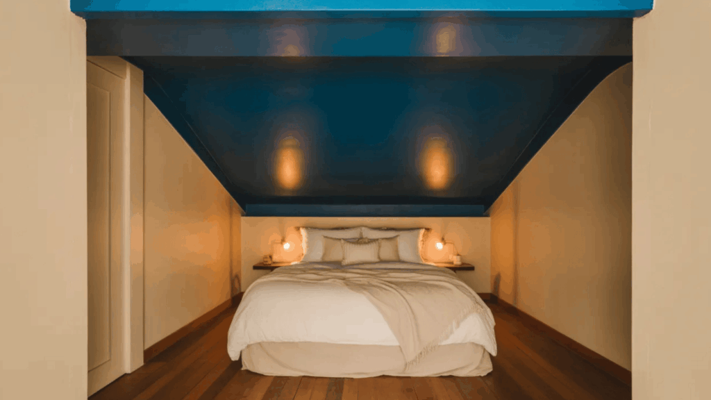 cozy bedroom with a blue sloped ceiling, beige bedding, and warm lighting from bedside lamps