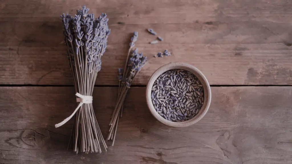 dried lavender bundle for display placed next to a bowl of stripped lavender buds on a wooden surface showing both storage options after drying