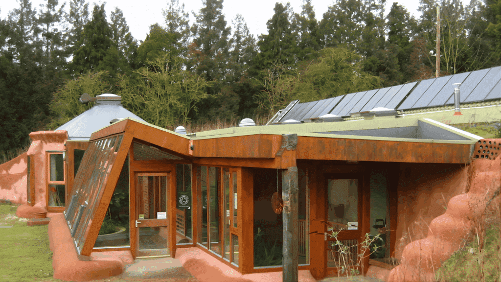 earthship style eco home made with natural and recycled materials featuring sloped glass windows solar panels and surrounding greenery