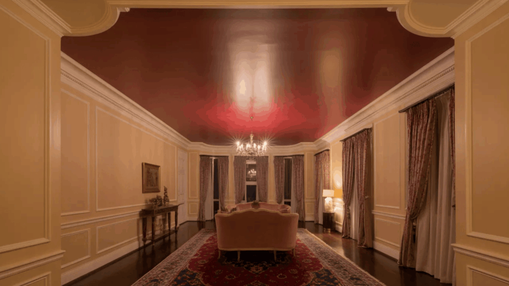 elegant living room with a deep red ceiling, chandelier, patterned rug, and ornate curtains