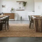farmhouse dining room with stained concrete floors, wooden furniture, and plants.