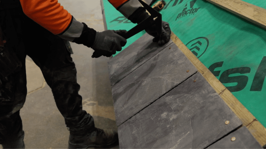 fixing slate tiles onto bottom of roof battens using hammer and nails during step by step slate roofing installation process