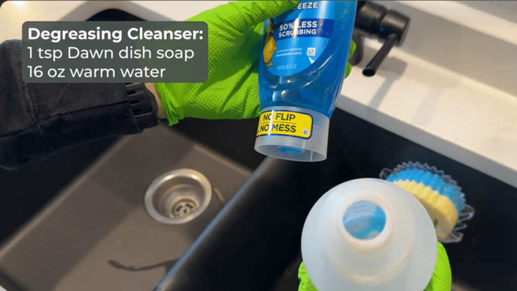 hand in green gloves pours blue dish soap into a bottle over a kitchen sink with sponge nearby and text showing cleaner recipe
