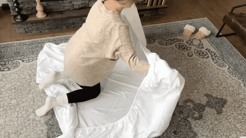 holding two corners of fitted sheet with hands inside seams while fabric hangs freely