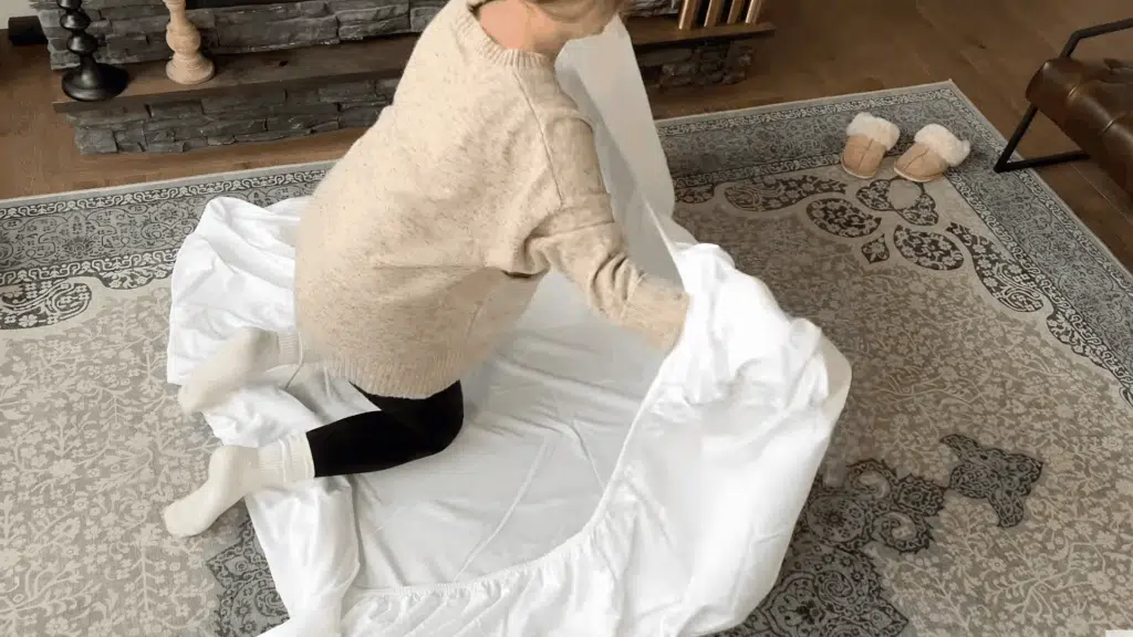 holding two corners of fitted sheet with hands inside seams while fabric hangs freely