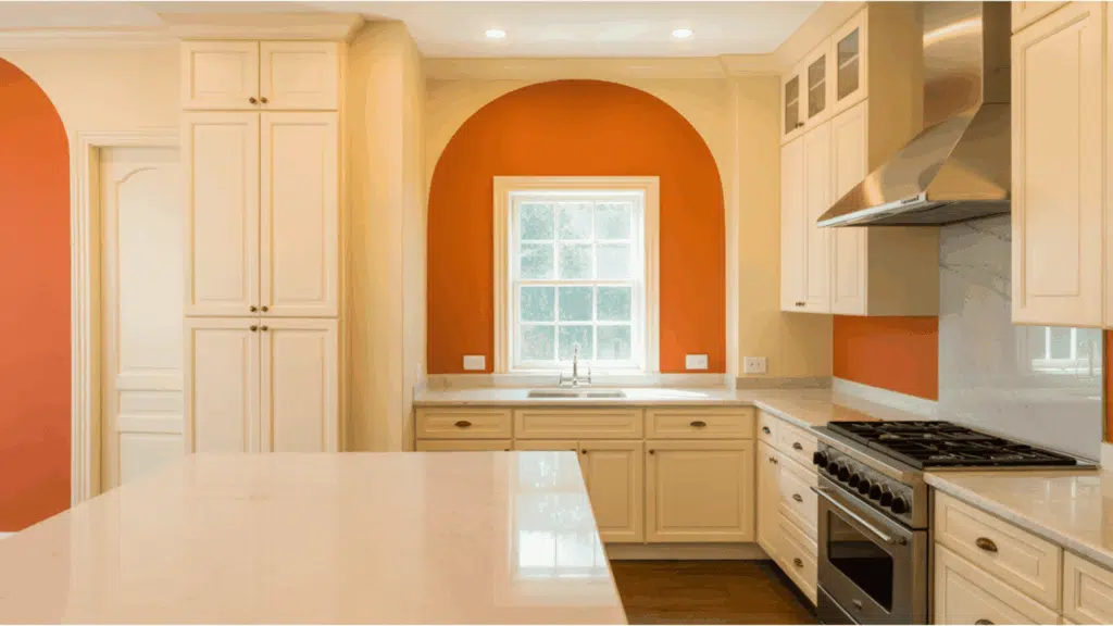 kitchen with cream cabinets and bold orange accent wall around the window.
