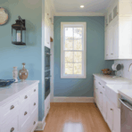 kitchen with sky blue walls, white cabinets, farmhouse sink, and natural light from tall window.