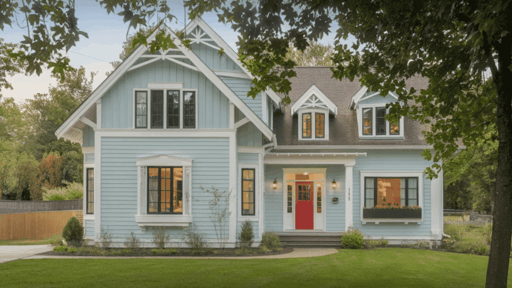 light blue house with white trim and a red front door, surrounded by trees and a neatly landscaped green lawn