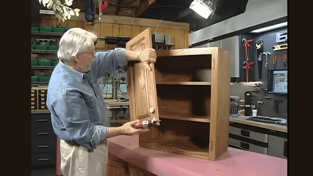 man removing cabinet door and hardware in a workshop for refinishing.