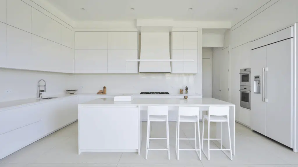 minimal all-white kitchen with large island, white cabinets, and modern bar stools.