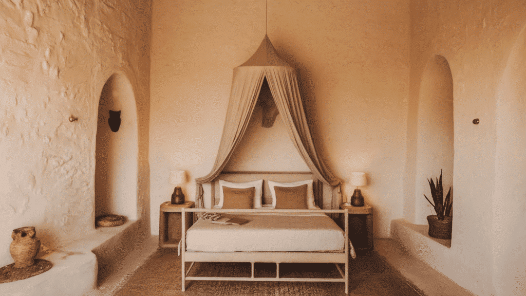 minimalist bedroom with white textured walls, a canopy bed, warm bedside lamps, and earthy decor