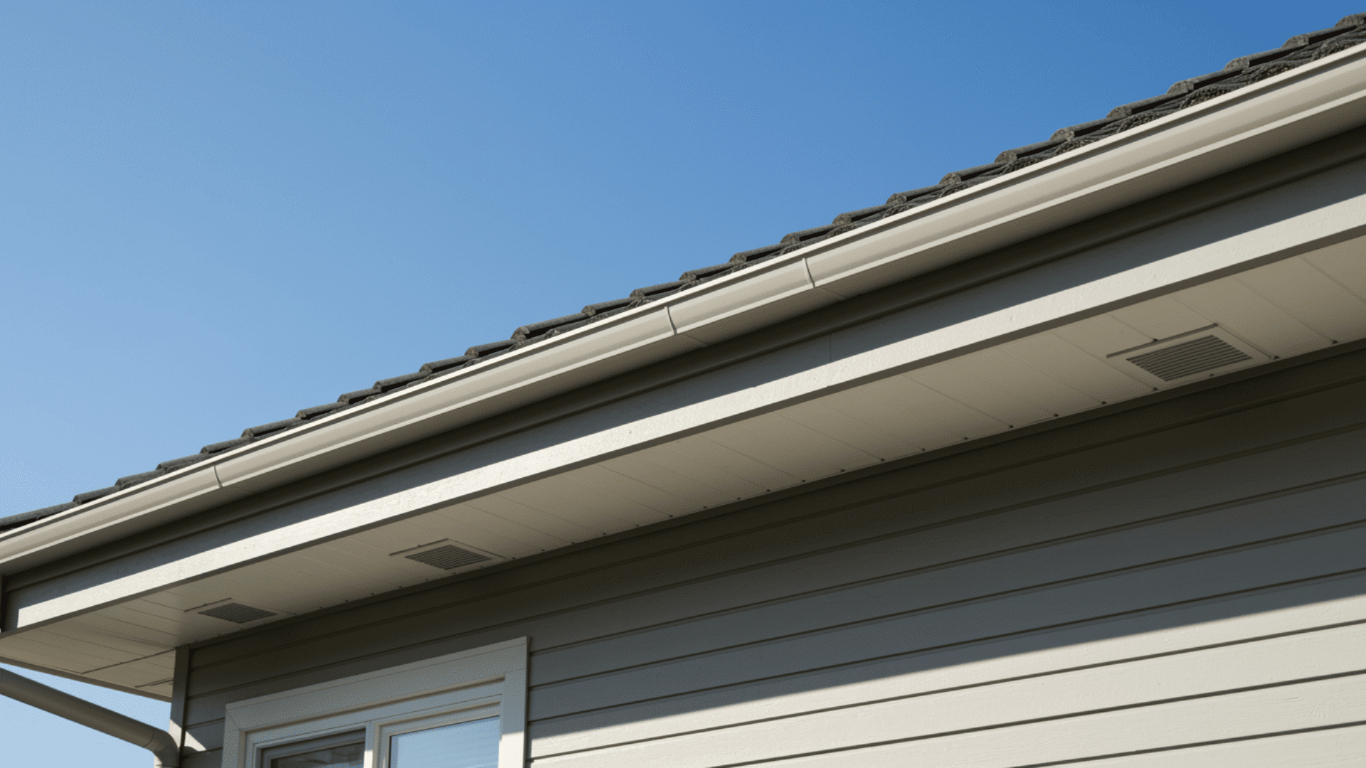 modern house roof with soffit panels under the eaves, showing ventilation grills, clean exterior siding, and a clear blue sky background