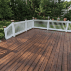 painting pressure treated wood deck with fresh stain finish and white railing in backyard surrounded by trees