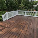 painting pressure treated wood deck with fresh stain finish and white railing in backyard surrounded by trees